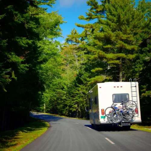 class C RV driving down a forested road
