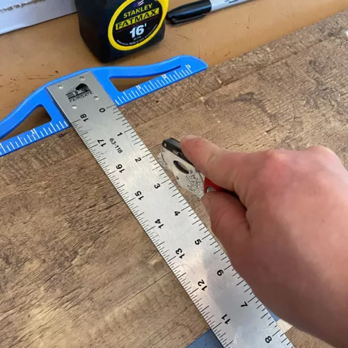 Hand scoring a vinyl plank with a T square and utility knife